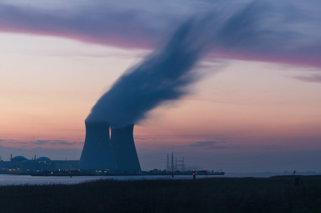 Two nuclear power station cooling towers on the shore of a river or sea. It is dusk.